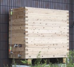 Amebits, the wooden tank, is used for watering a flower bed by collecting rainwater.